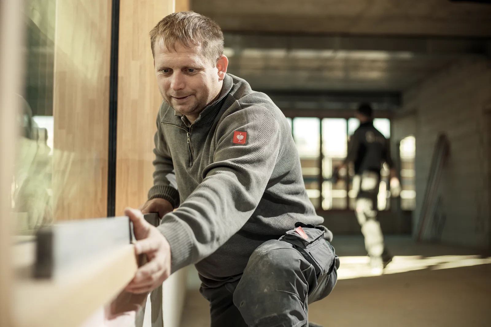 Heigl-Monteur bei der Montage eines Holz-Alu-Elements, lächelnd bei der Arbeit