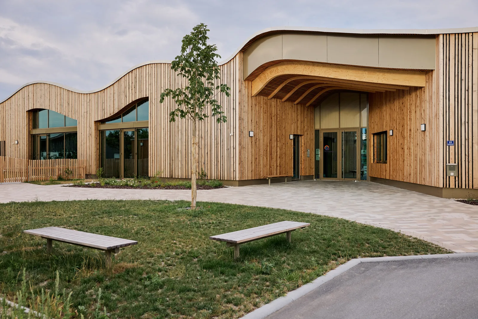 Kita Unterm Regenbogen in Dingolfing — geschwungener Baukörper mit Holz-Aluminium-Fassadenelementen und großen Verglasungen am Eingang