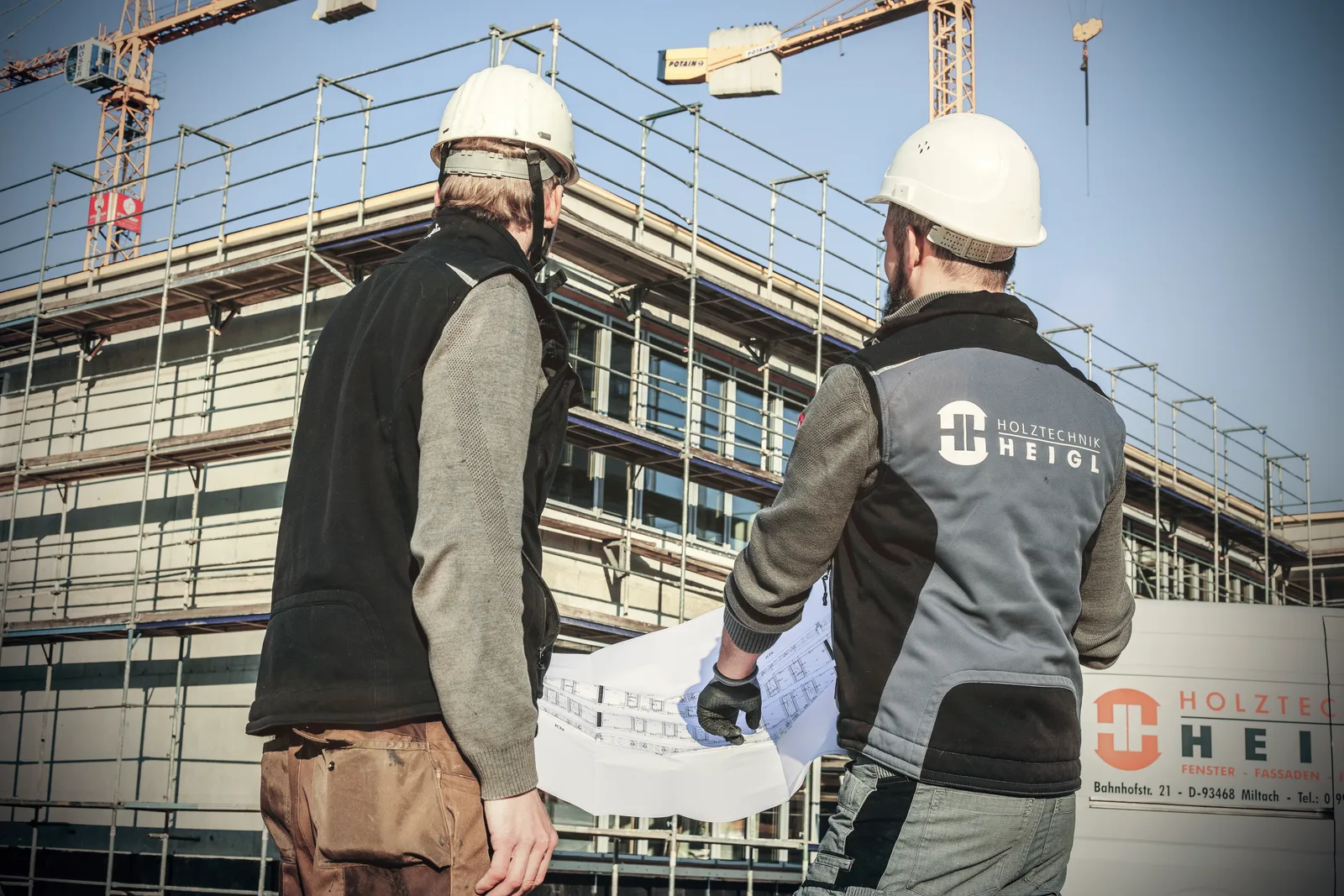 Zwei Heigl-Monteure mit Plan vor der eingerüsteten Fassade