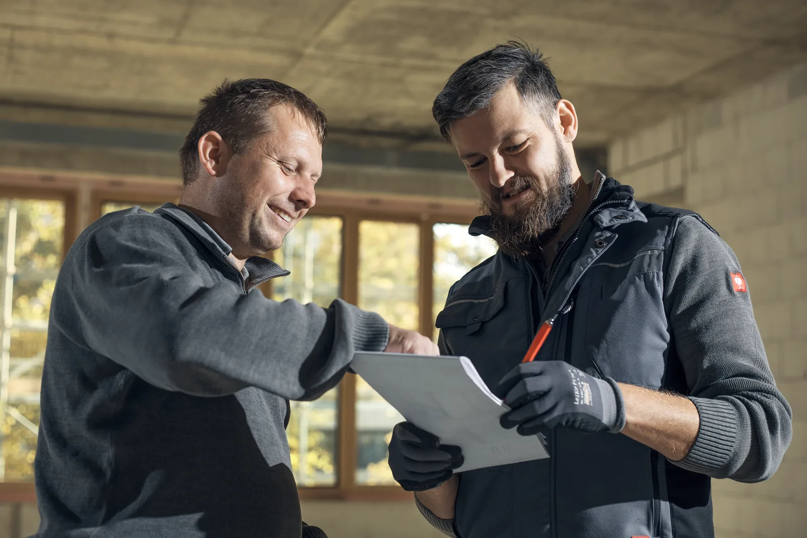 Zwei Heigl-Kollegen besprechen lachend die Montage-Checkliste auf der Baustelle